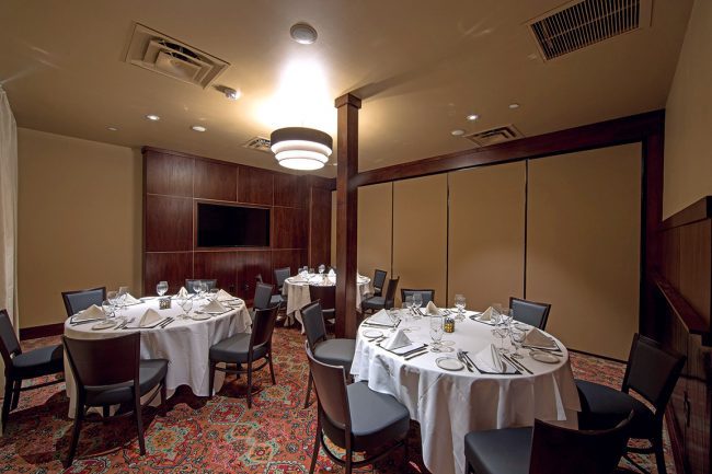 Truluck's Arboretum Capri room view from entry door, 3 round tables and TV on wall is showing