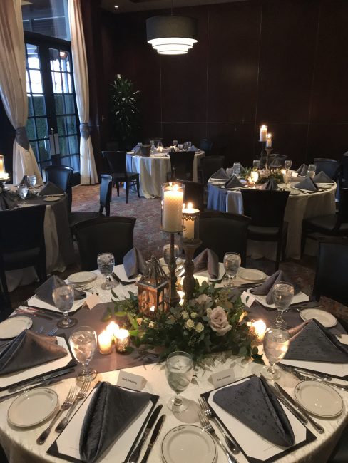 picture of Truluck's Woodlands private event with shabby chic centerpieces to include a lantern, pillared candles and whimsical greenery with light pink roses. Napkins are a navy accent with navy table runner.