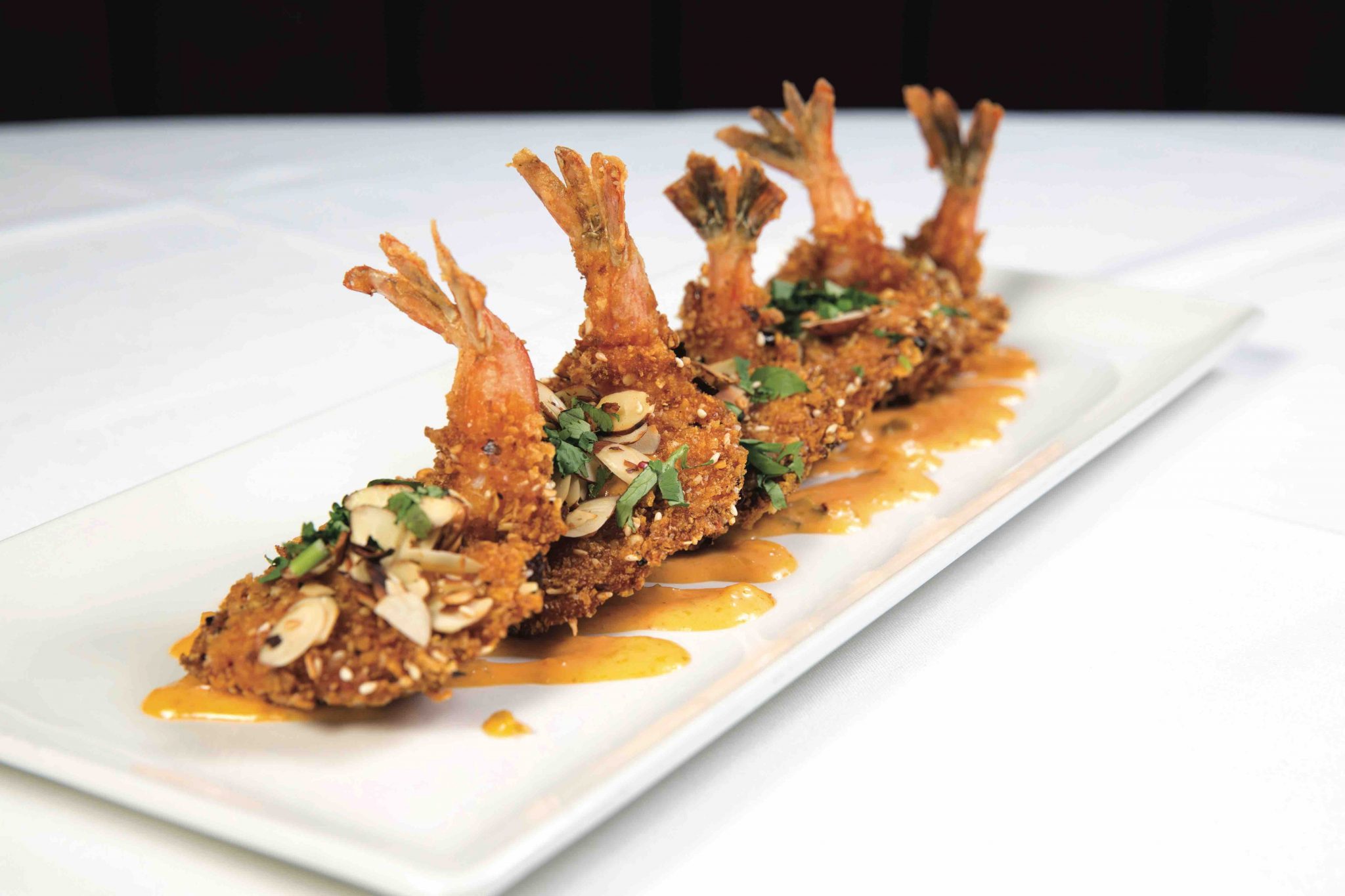 Breaded shrimp, sprinkled with fresh parsley and almond shavings and sitting on top of a bed of spicy orange sauce