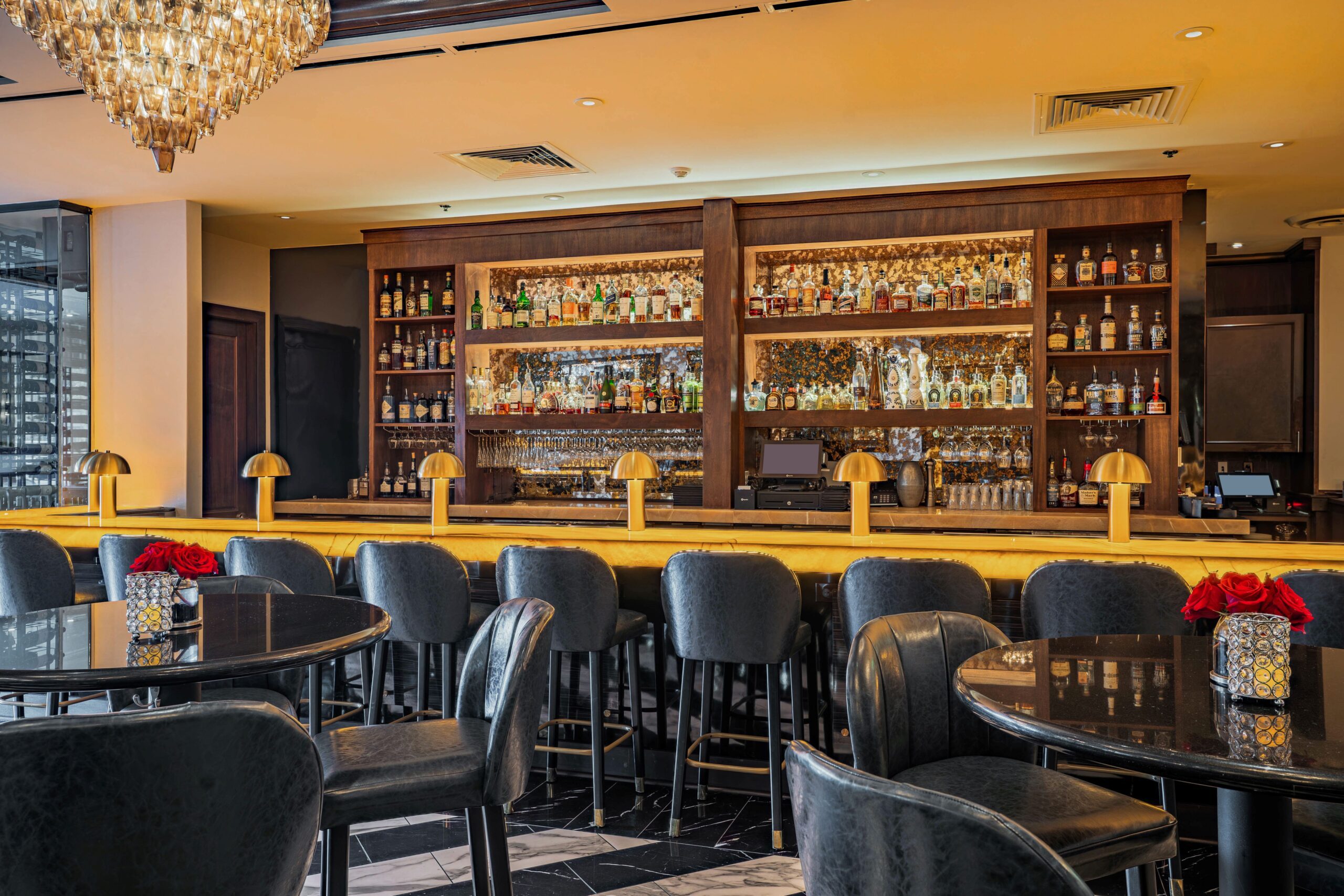 High-end bar setting at Truluck’s Houston featuring a glowing gold bar, elegant lighting, leather seating, and an extensive collection of premium spirits.