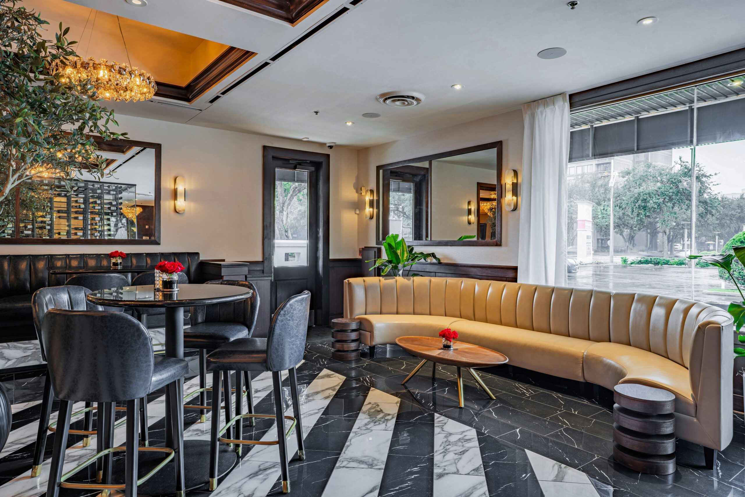 Stylish lounge at Truluck’s Houston with marble flooring, curved cream banquette, indoor olive tree, and contemporary seating surrounded by natural light.