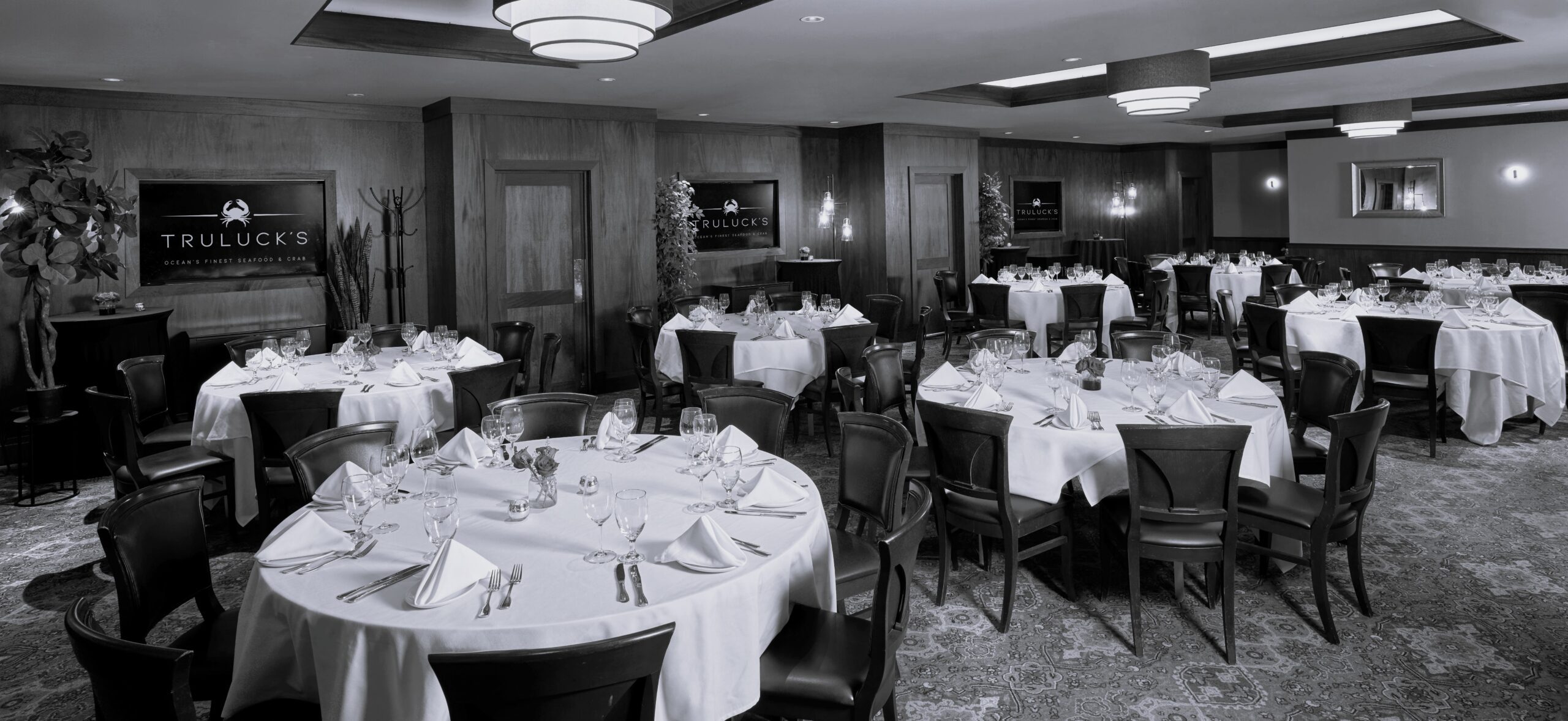a large private dining room with a mix of round tables draped in white tablecloths with polished glassware and floral centerpieces. The walls are a mix of mahogany wainscot with