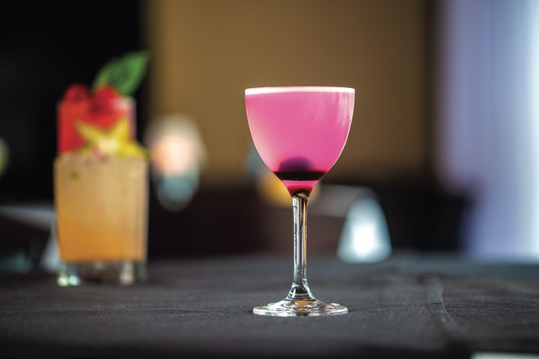 Bright pink drink in a stemmed cocktail glass with a berry in the bottom