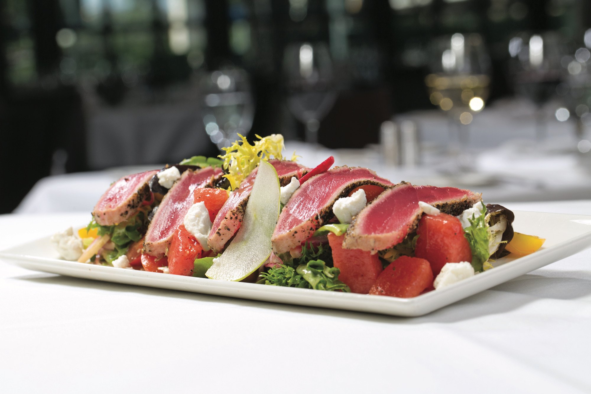Pepper-crusted tuna lying on top of greens, tossed with watermelon, tomato, shaved red onions, and goat cheese
