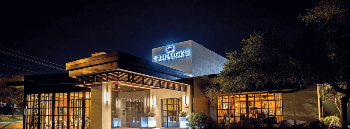 Truluck's restaurant in the nightime, lit with warm light from the inside and with a glowing logo 