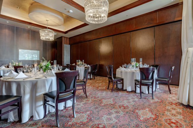 The Naples room at The Woodlands location setup with white linen draped tables, crystal chandeliers and mahogany wood chairs