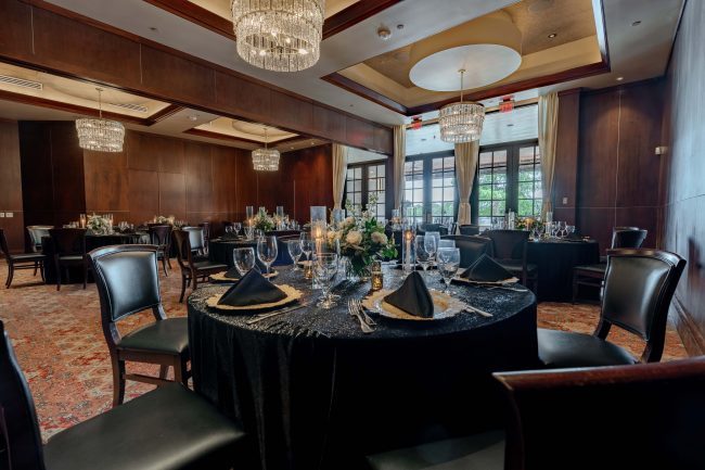 The Stone Crab Room at The Woodlands location. View from the corner. Round tables dressed in black table cloths with mahogany wood chairs and glass French doors overlooking the terrace.