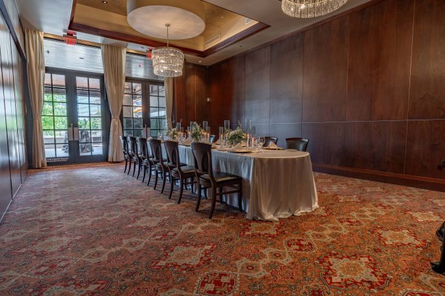 The Naples room at the Woodlands location set up with a long rectangular table dressed in white linen with glassed in French doors overlooking the terrace.