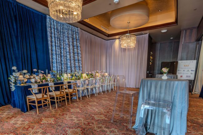 The Stone Crab room at The Woodlands dressed with blue and white pattern pipe and drape, a long rectangular table, chivari chairs and floral centerpieces