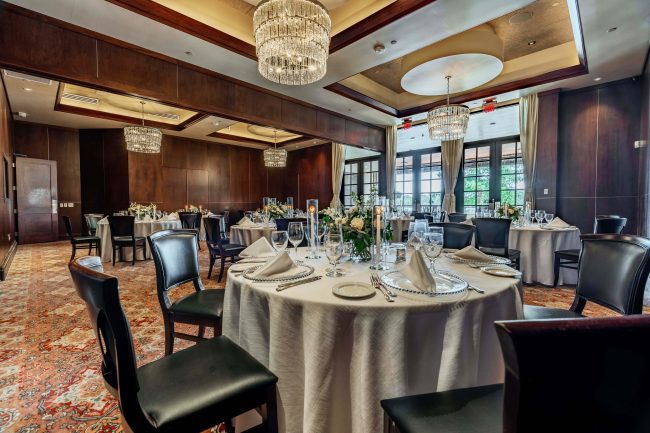 The Stone Crab Room at The Woodlands location. White linen table cloth draped tables with full place settings, mahogany wood chairs, crystal chandeliers and windowed French doors.