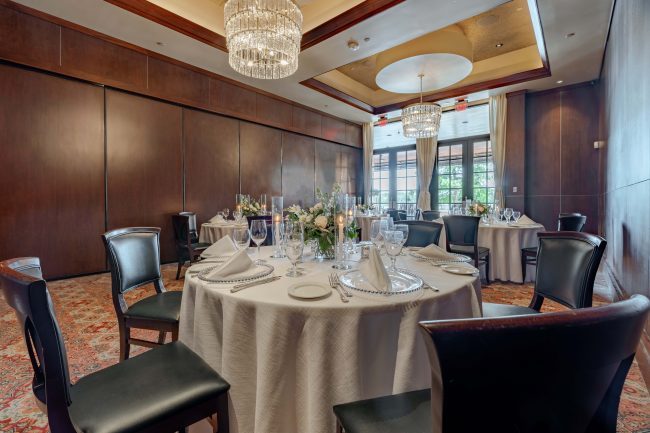 The Naples room at the Woodlands location set up with round tables dressed in white linen with glassed in French doors overlooking the terrace.