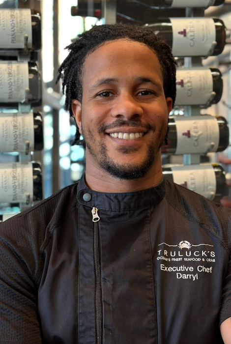 Chef Darryl of Truluck's DC in a black chef coat standing in front of the wine wall