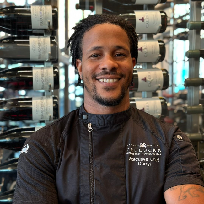 Chef Darryl of Truluck's DC in a black chef coat standing in front of the wine wall