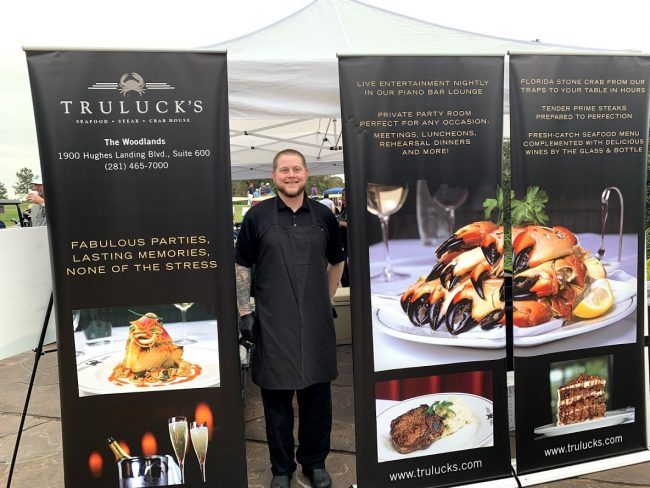 Chef Partner Shane Flynn at an offsite charity event standing next to the Truluck's banners.