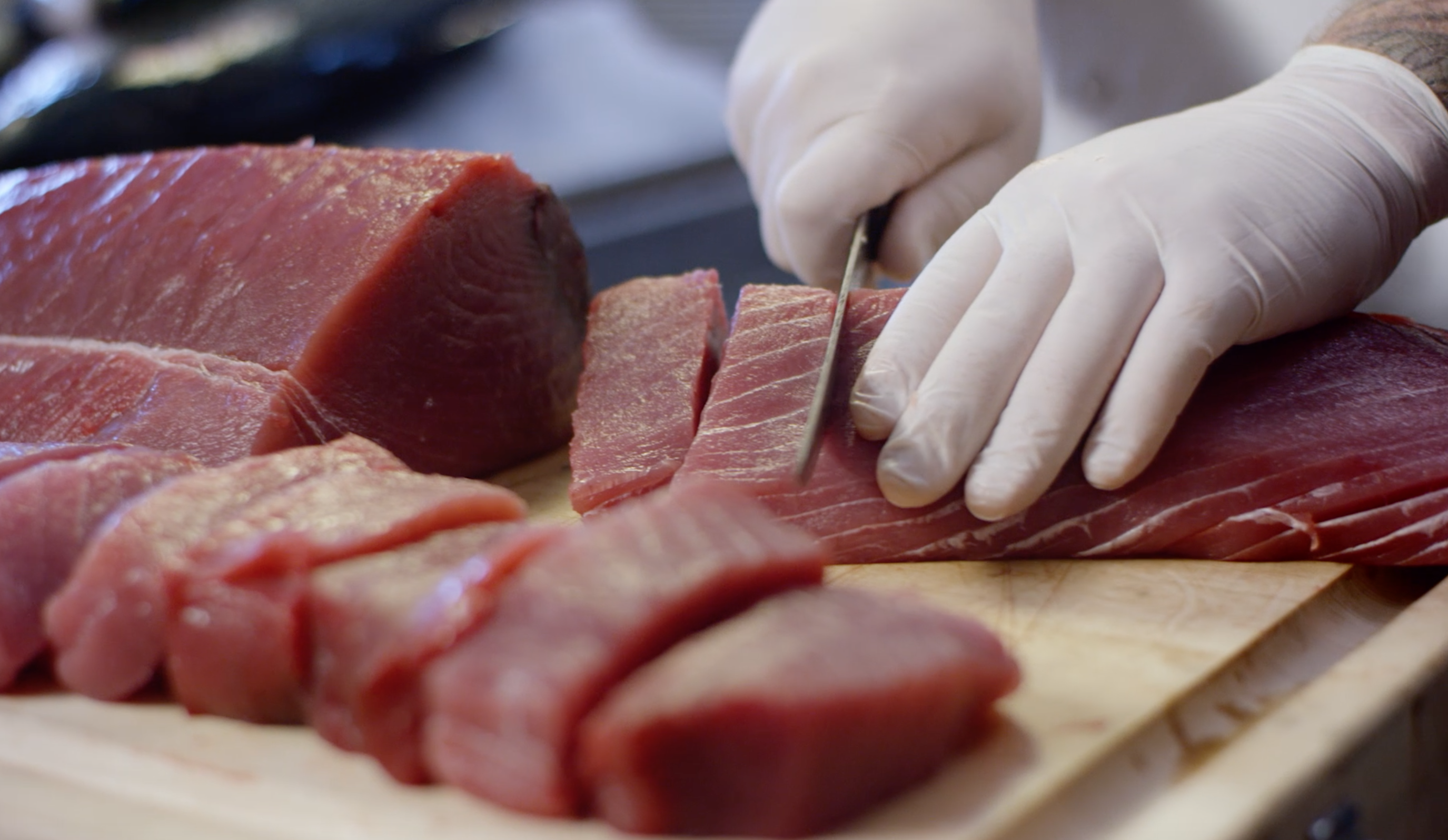 Chef cutting fresh ahi tuna on a cutting board with gloved hands.
