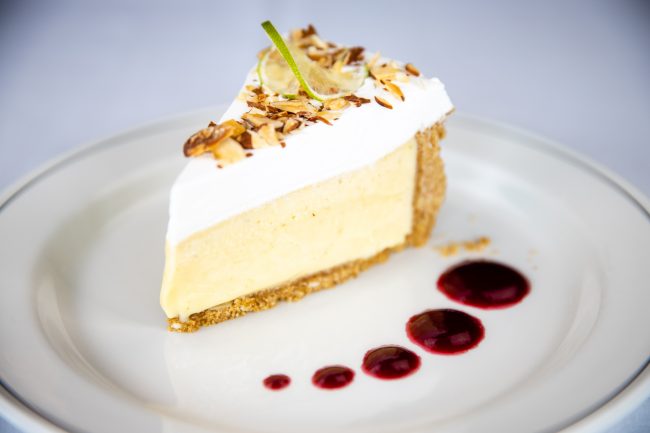 picture of key lime pie topped with slivered almonds on a plate with fresh raspberry sauce