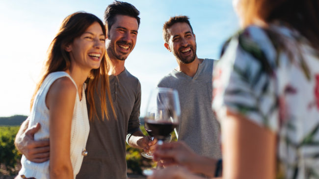 picture of group of people smiling and holding wine glasses in a vineyard