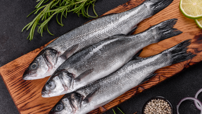 picture of whole seabass fish on a cutting board with fresh herbs and lime wheels