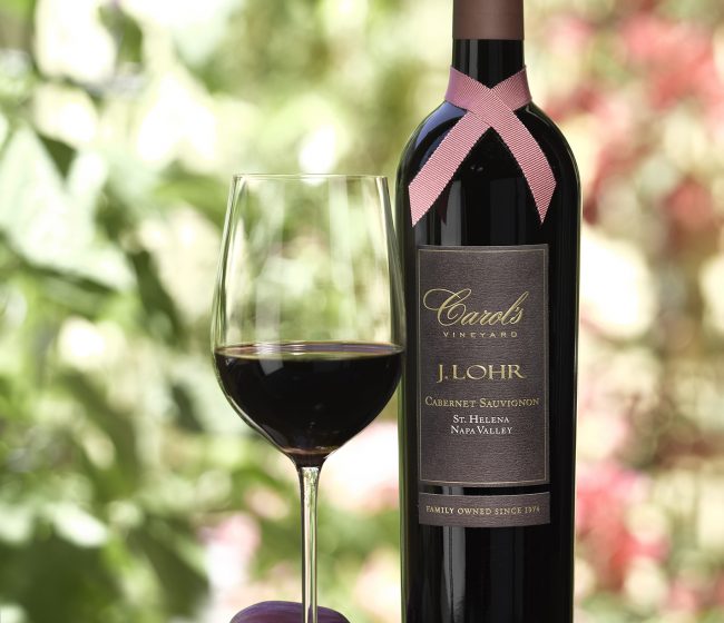 picture of the J. Lohr Carol's Vineyard cabernet wine bottle with a pink ribbon wrapped around the bottle neck and a glass of red wine.