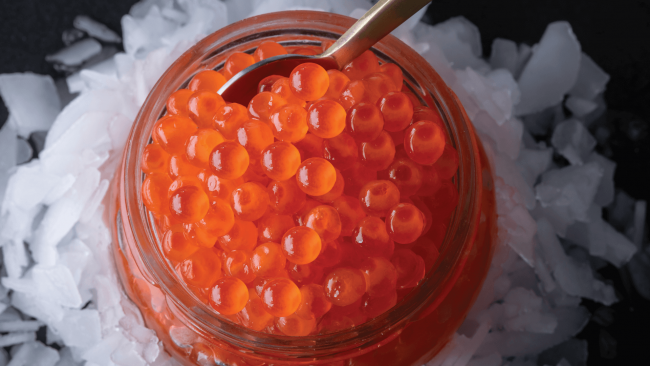 picture of an opened jar of Ora King caviar with a spoon in the jar atop a bed of ice