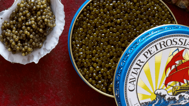 picture of Caviar Petrossian in a tin with an oyster shell filled with caviar next to the tin.