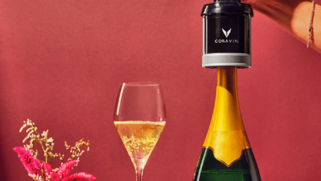 picture of the Coravin wine sparkling system cap on a green and gold bottle of champagne with a glass of champagne against a pink background.
