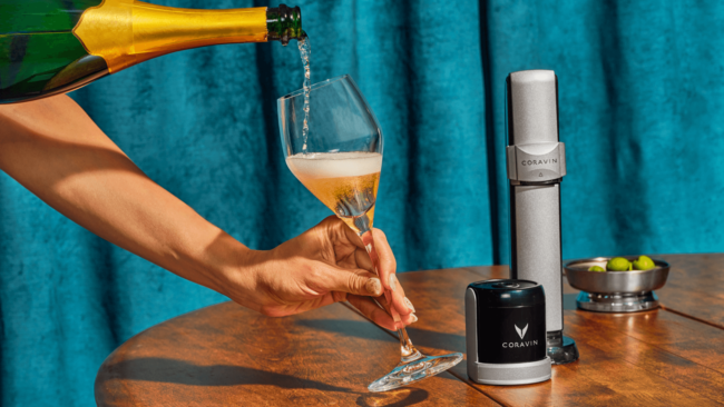 Photo of Coravin wine sparkling system with a woman holding a glass and pouring champagne from a green and gold champagne bottle