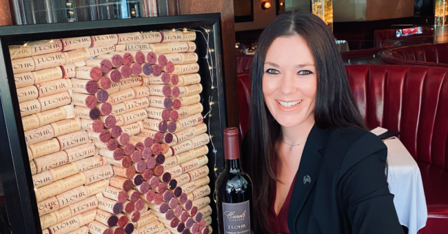 picture of Megan Holt with the J. Lohr wine cork board she made that features a breast cancer ribbon made of corks