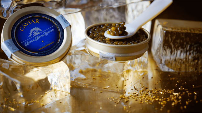 picture of Black River Caviar tin on ice with a pearl spoon and shaved gold flakes