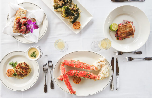 an overhead picture of a table setting with king crab, halibut, broccoli, tuna crudo, crab cake