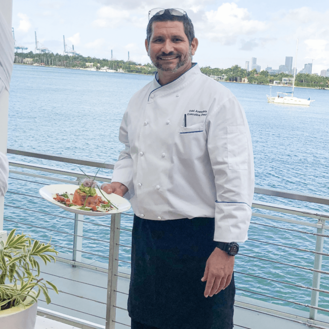 picture of Chef Odel holding an entree with he ocean in the background