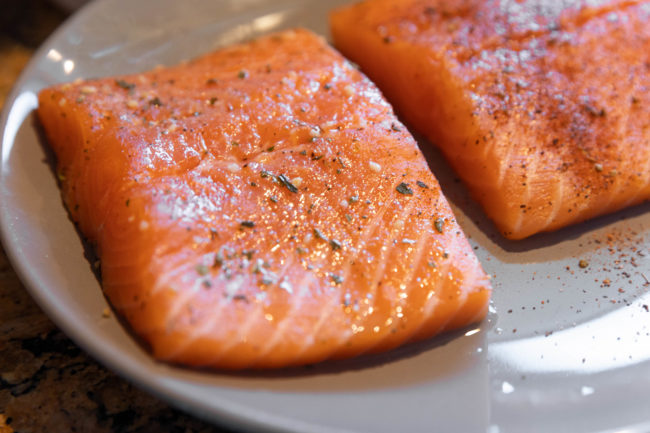 picture of two uncooked filets of salmon topped with garlic and herb seasoning