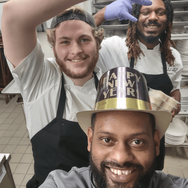 Chef Ricardo wearing a Happy New Year Hat and a few line cooks on New Year's Eve