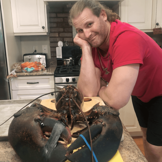 photo of Chef Travis with an enormous lobster he's getting ready to cook in his kitchen