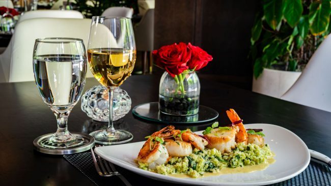 scallop and shrimp saute entree over cauliflower florentine with a vase of red roses and a glass of white wine in the background