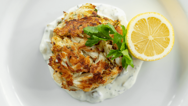 jumbo lump crab cake over tartar sauce with a fresh half of a lemon and parsley leaf