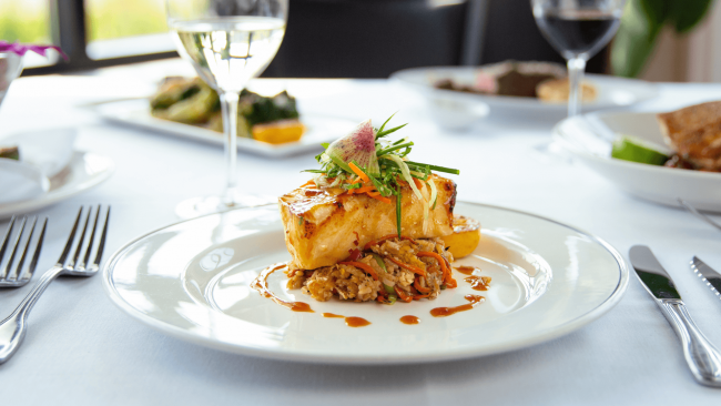 a photo of miso glazed seabass with crab fried rice and cucumber slaw with a glass of wine in the background