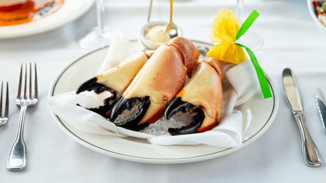 Three large fresh Florida stone crab claws on a plate with a ramekin of mustard and a wrapped lemon