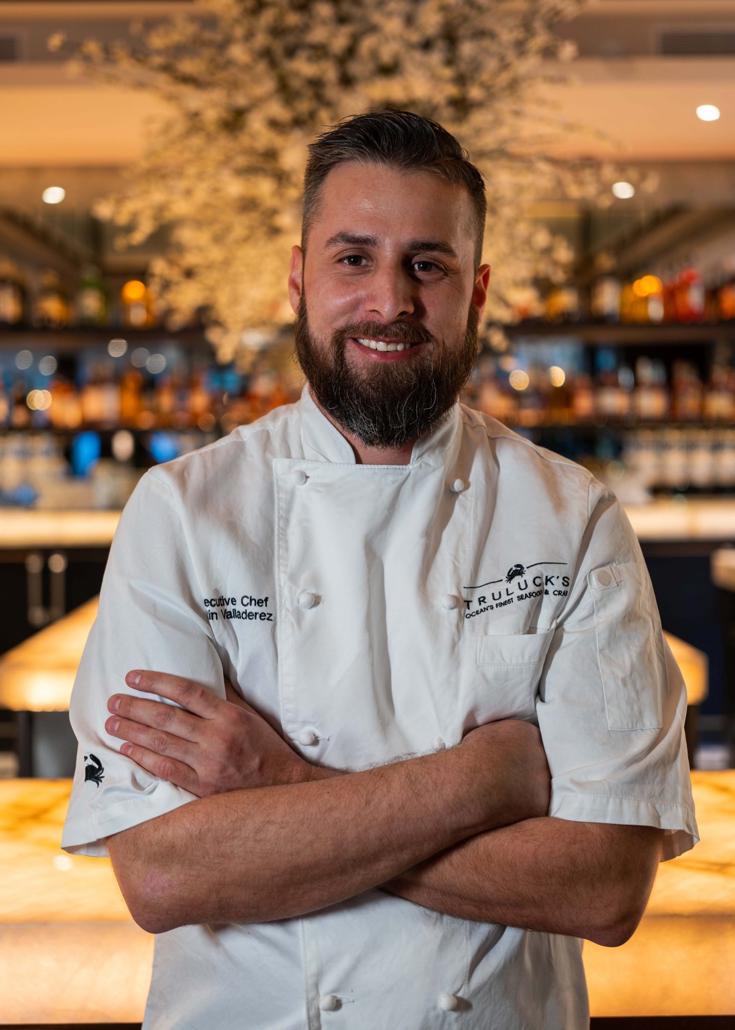 photo of Chef Justin at the Truluck's Plano location in front of the bar with his chef coat on and arms crossed on his chest