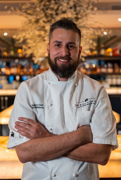 photo of Chef Justin at the Truluck's Plano location in front of the bar with his chef coat on and arms crossed on his chest
