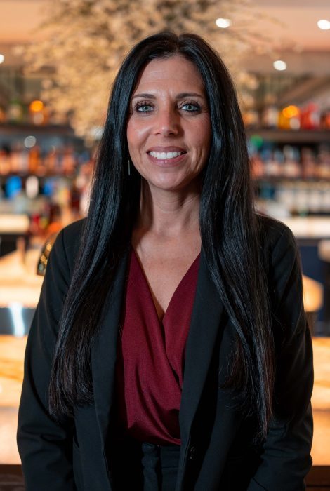 photo of Truluck's Plano general manager, Tambra Tatum, in a black suit jacket with maroon blouse in front of the bar
