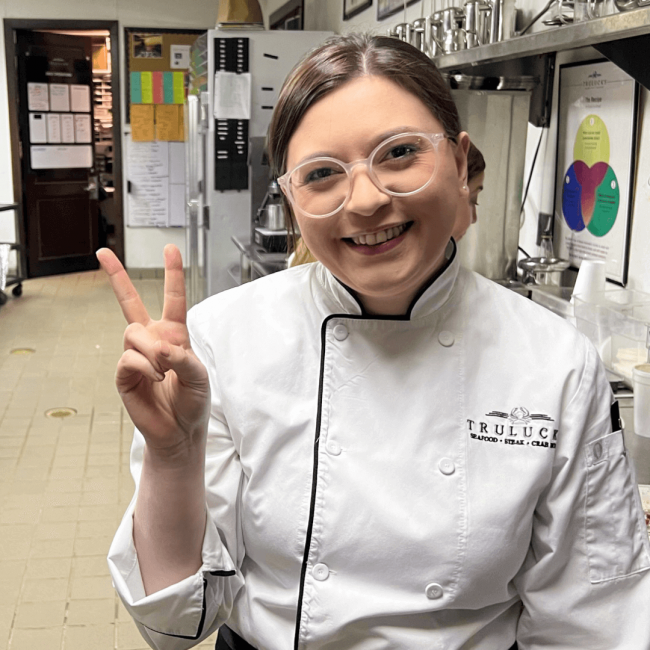 Truluck's server holding her hand in a peace sign in the kitchen area