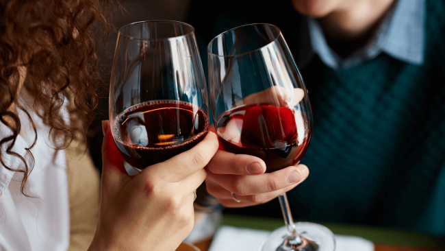 photo of a man and woman's hands toasting with glasses of red wine