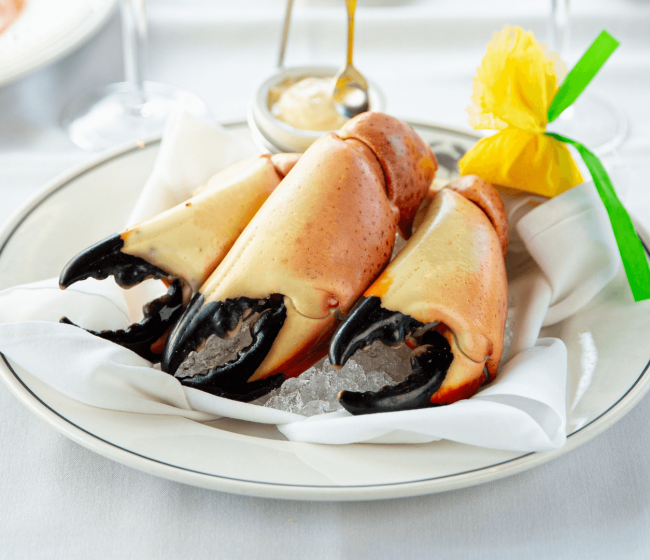 three jumbo Florida stone crab claws on a bed of ice on a plate with a wrapped lemon