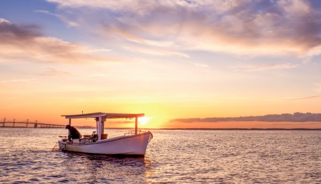 crab fishing boat in the ocean with a bridge and the sunset in the background