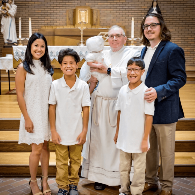 Marinella and her family at her baby's baptism in the church with the priest