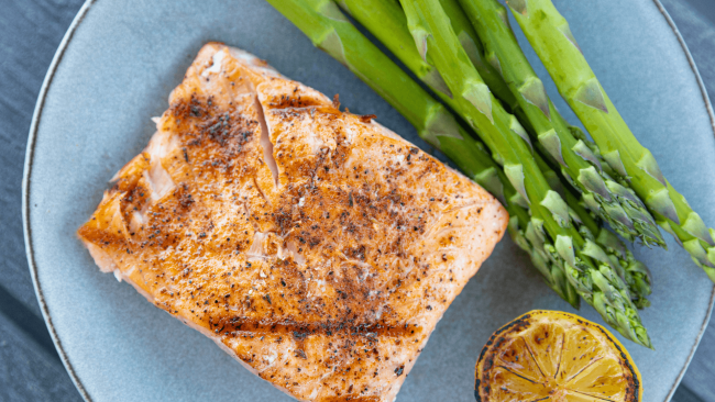 photo of a cooked salmon filet with asparagus spears and a grilled lemon