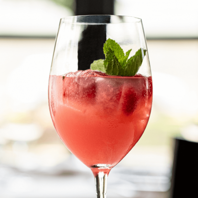 picture of the Summer Romance cocktail filled with ice, fresh raspberries and mint in a wine style glass