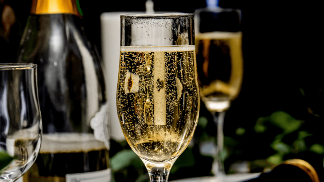 a glass of bubbly champagne with a bottle of champagne in the background and another glass in the background