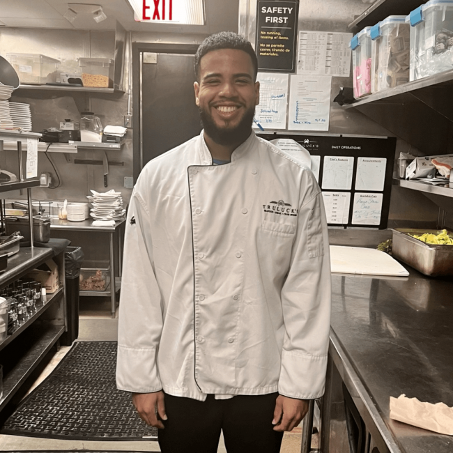 phot of server, Mario, in the back of house kitchen area smiling and getting read for the shift